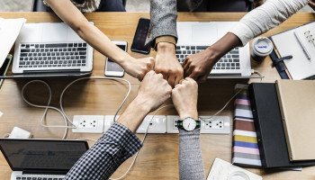 People bumping fists around a table in support / congratulations.