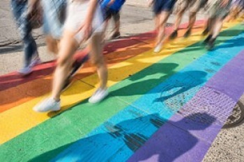 Image of rainbow coloured crossing track and blurred people's legs walking on it